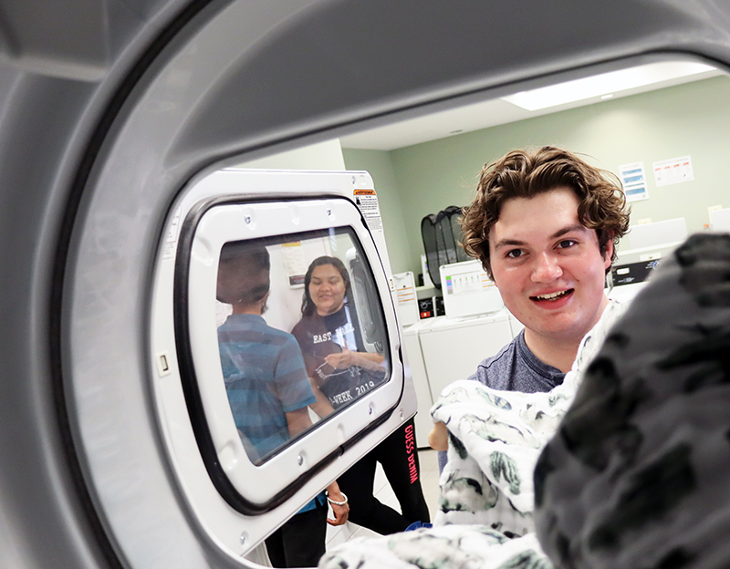 photo of students chatting in laundry area through dryer view