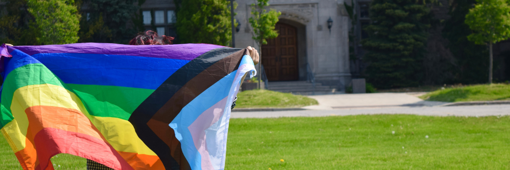 A student holding a Pride Flag outside Johnston Hall.