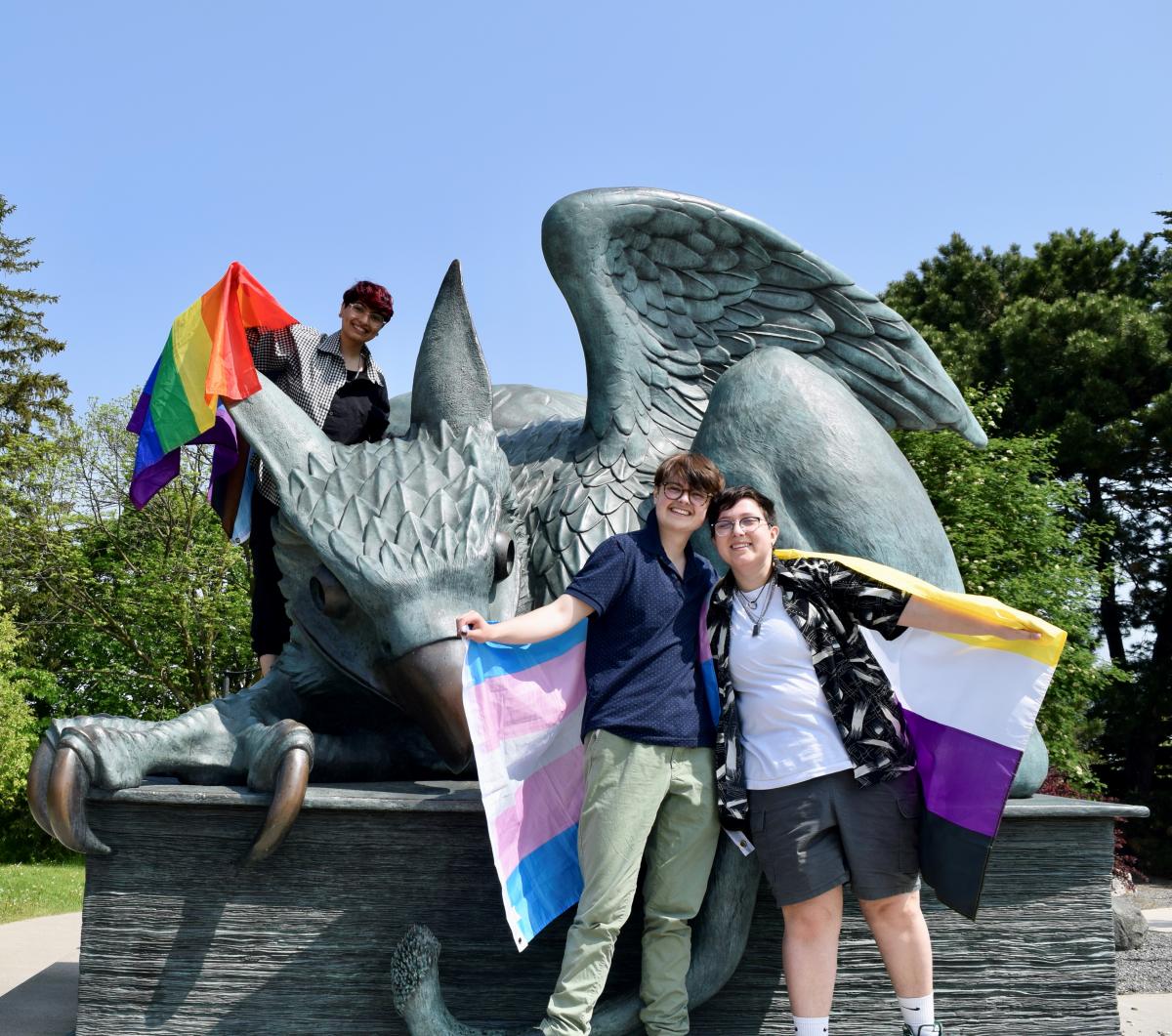 Three students at the Gryphon Statue holding Pride Flags