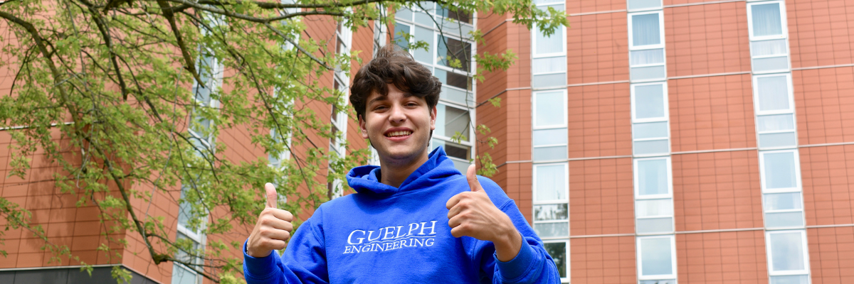 Student smiling with thumbs up in front of Addington Hall. 